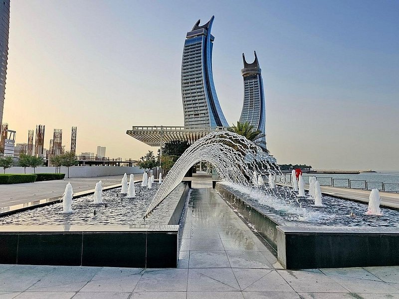 A waterfront fountain in Doha with the curved Lusail towers behind it